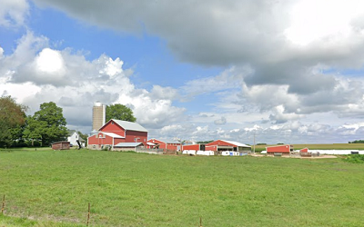 Red farm buildings with blue sky and white clouds and green pasture in front