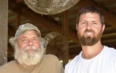 Two male farms who are smiling while standing under a barn